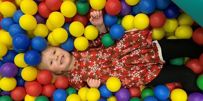 Little girl smiling and playing in color ball pit. 