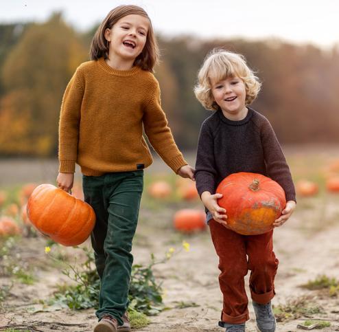 Two kids picking out pumpkins in a pumpkin patch.