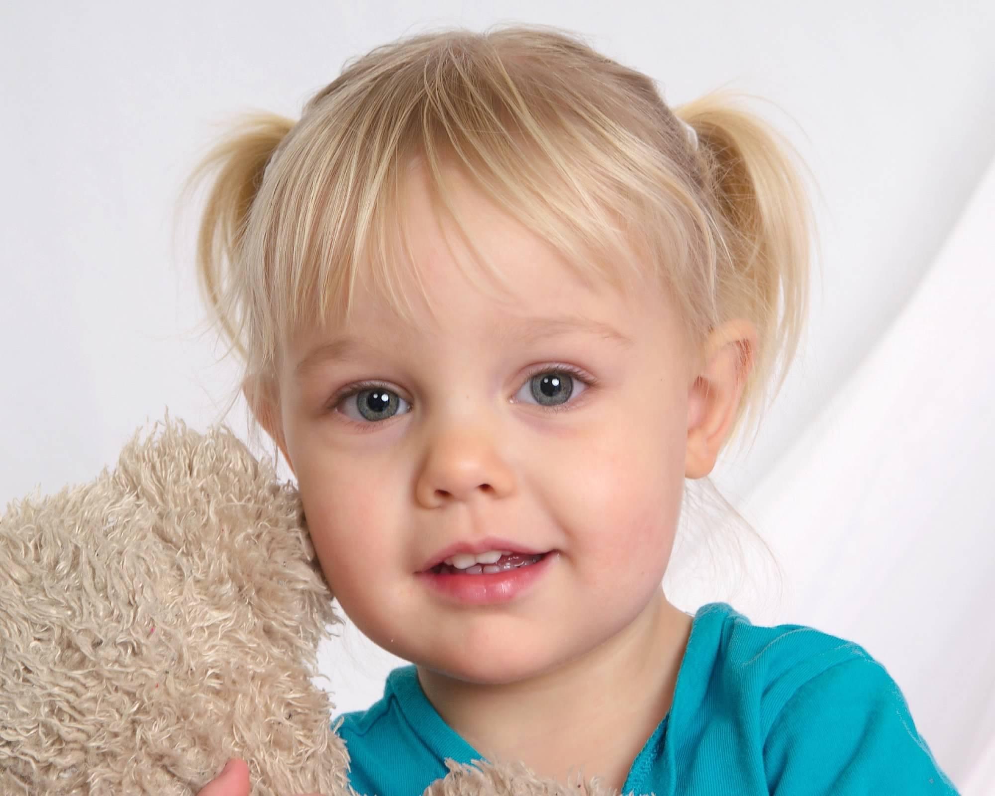 toddler with blonde hair in pigtails holding light brown teddy bear